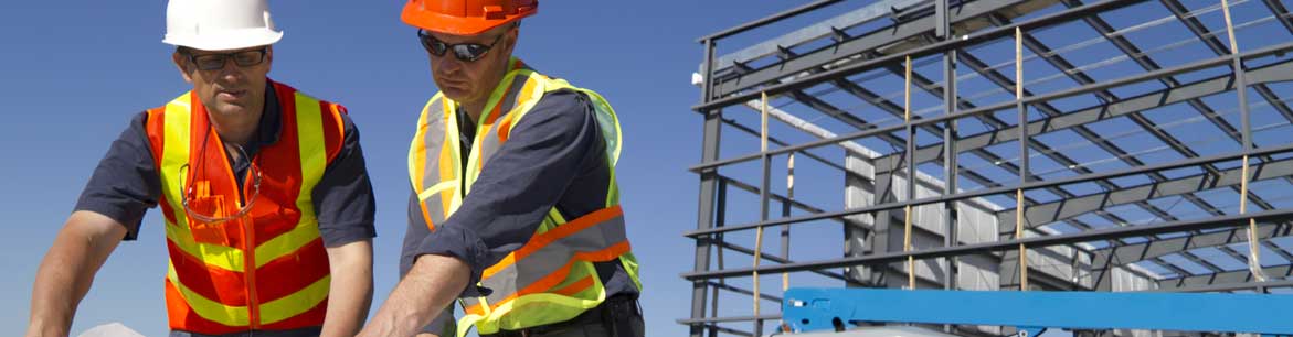 Two workers on site reviewing blueprints.